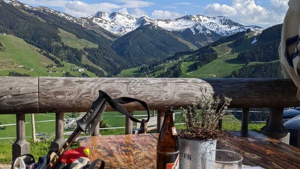 Une table avec une bouteille de bière et un verre, un sac à dos et une plante, donnant sur un paysage montagneux.