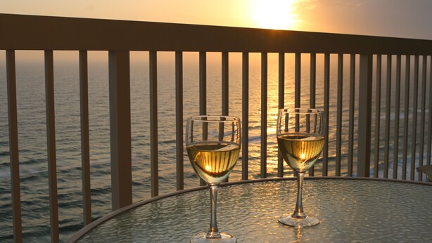 Zwei Gläser Weißwein auf einem runden Tisch mit Blick auf das Meer und einen Sonnenuntergang.
