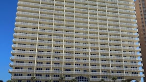 Ein Hochhaus-Hotel mit mehreren Balkonen und einem Strandbereich mit Sonnenschirmen und Liegestühlen.