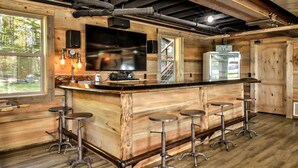 Un coin bar rustique en bois, doté d’un grand téléviseur, de tabourets de bar et d’un réfrigérateur.
