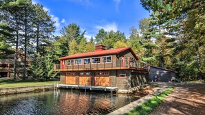 Une cabane à deux étages avec un quai s’avançant dans un étang, le tout entouré d’arbres.