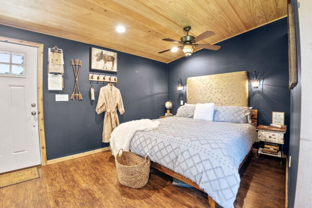 Une chambre avec un plafond en bois, un lit recouvert d’une couvre-lit à motifs, une table de chevet avec une lampe et une horloge fixée au mur.
