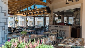 An outdoor dining area with wooden tables and chairs, hanging plants, and a bar area with bottles. - Windmill Hotel (Zakynthos)