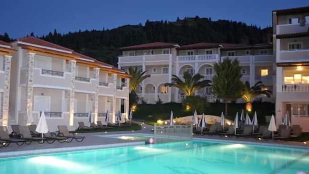 A hotel with a swimming pool, multiple balconies, and a mountainous backdrop. - Windmill Hotel (Zakynthos)