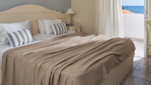 A hotel room with a bed, a nightstand, a lamp, and a view of the sea through a window. - Windmill Hotel (Zakynthos)