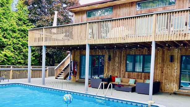 Une terrasse en bois avec une piscine, un espace salon extérieur et un escalier menant à un deuxième niveau.