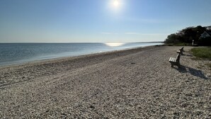 Une plage de galets avec deux bancs en bois donnant sur la mer.