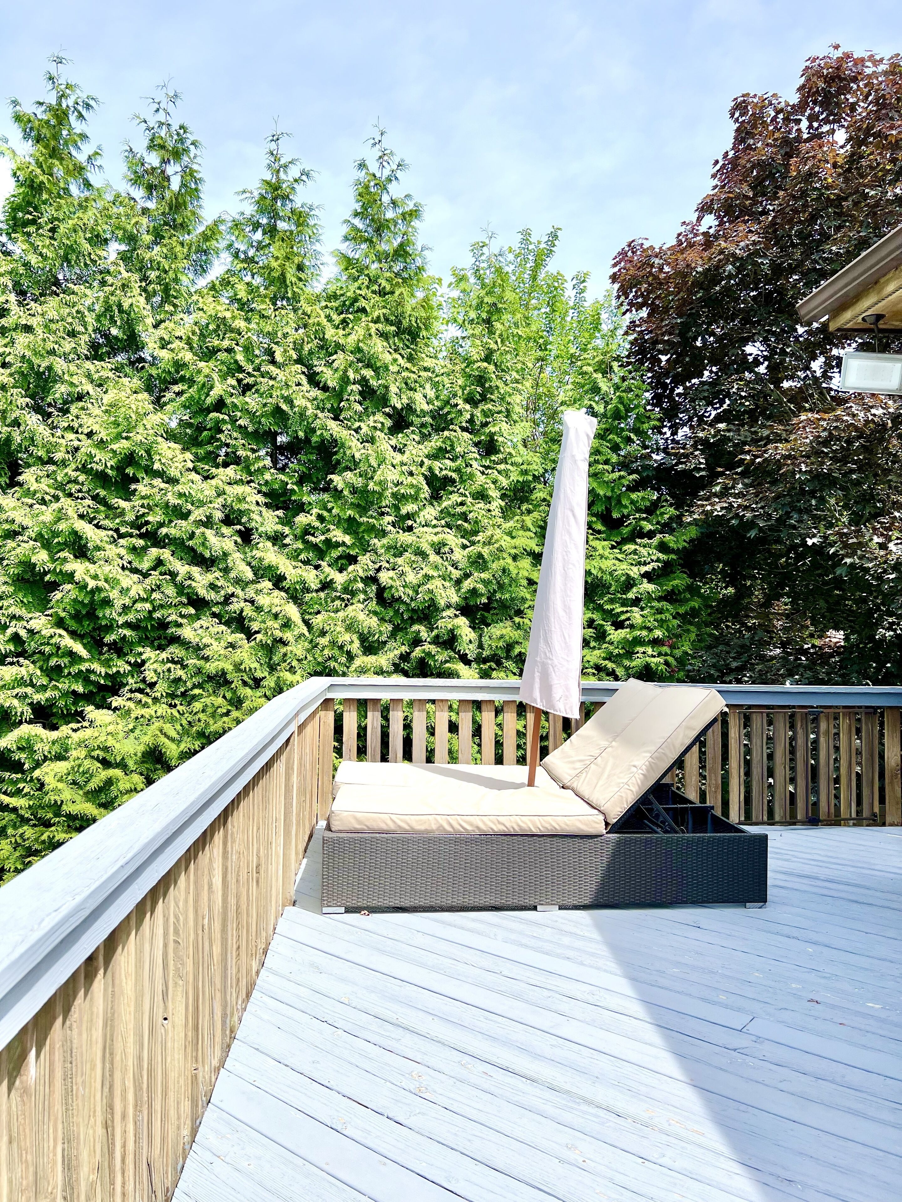 Una terraza de madera con una zona de estar acolchada y una sombrilla blanca.