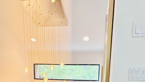 Un escalier avec une rampe en bois, un luminaire suspendu doté de plusieurs ampoules et une fenêtre donnant sur un paysage verdoyant.