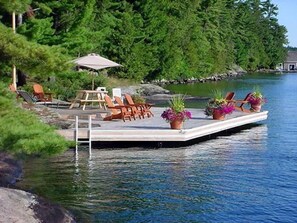 A dock with chairs and potted plants, surrounded by water and greenery.