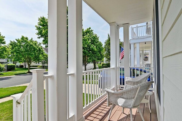 A covered porch with white railings, a wicker chair, and a hanging plant.