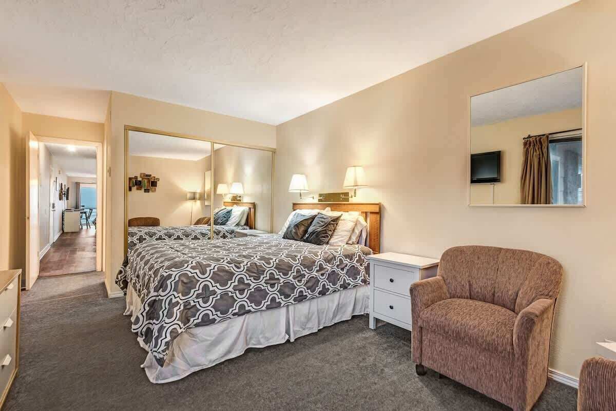 Een hotelkamer met een groot bed, nachtlampjes, een stoel, een televisie en een spiegel.