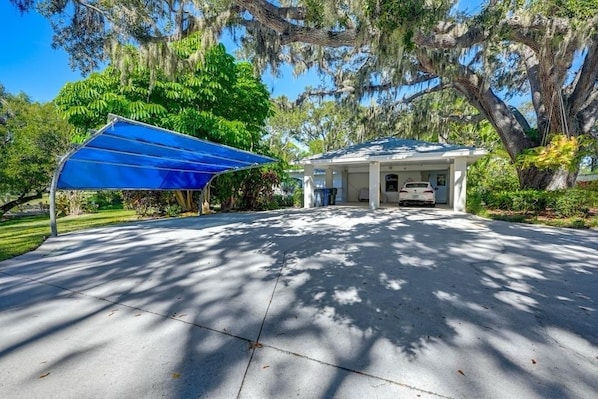 A covered garage with a car parked inside, surrounded by trees and greenery. - Peaceful And Private Unit, With Cover Parking (Sarasota)
