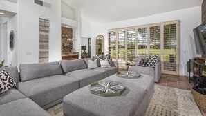 A spacious living room with a grey sectional sofa, a coffee table with a geometric pattern, and a large sliding glass door leading to a patio. - Relax in the Best and Biggest Space in Palm Valley Country Club. (Palm Desert)