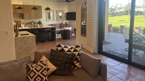 A modern living room with a sofa, a dining area with a kitchen in the background, and a sliding glass door leading to a patio. - Relax in the Best and Biggest Space in Palm Valley Country Club. (Palm Desert)