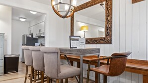 Un coin repas avec une table en bois et quatre chaises, un grand miroir décoratif et, au fond, une cuisine moderne.