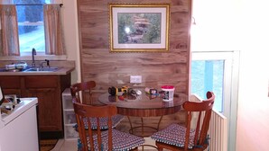 Un comedor con una mesa redonda y cuatro sillas de madera con cojines estampados. Encima de la mesa, cuelga un cuadro enmarcado.