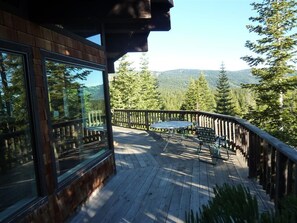 A wooden deck with a table and chairs, overlooking a forested area with mountains in the distance. - Large Home, Lovely Lake Views, Great Getaway (Tahoma)