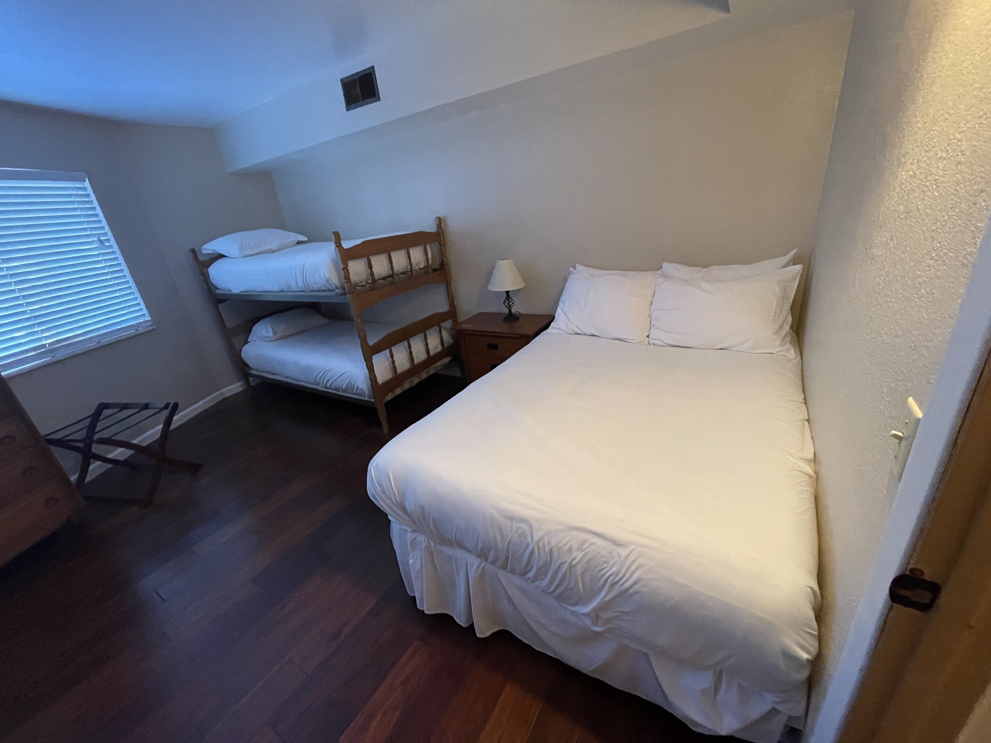 A bedroom with a large bed, a smaller bed, a wooden chair, a nightstand, and a window with blinds.