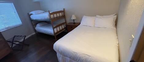 A bedroom with a large bed, a smaller bed, a wooden chair, a nightstand, and a window with blinds.