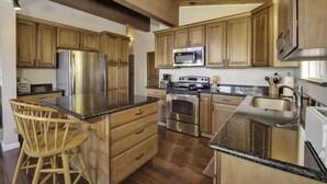 A kitchen with wooden cabinets, stainless steel appliances, a granite countertop, and a wooden island with a chair. - Large Home, Lovely Lake Views, Great Getaway (Tahoma)