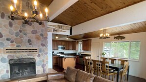 A spacious living area with a stone fireplace, leather sofa, wooden bench, and a dining area with wooden chairs and a table. - Large Home, Lovely Lake Views, Great Getaway (Tahoma)