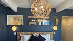 Un dormitorio con una cama grande, una lámpara decorativa en el techo, espejos en la pared y cuadros enmarcados.
