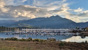 Un puerto deportivo con barcos amarrados, rodeado de montañas y una masa de agua.