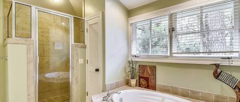 A bathroom with a walk-in shower, a bathtub, and a window with blinds.