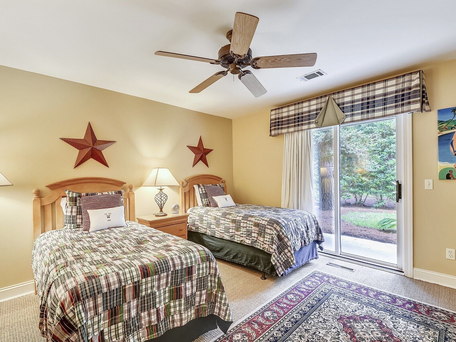 A bedroom with two beds, a ceiling fan, and a large window with a view of the outdoors.