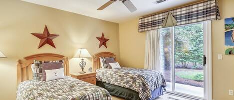 A bedroom with two beds, a ceiling fan, and a large window with a view of the outdoors.