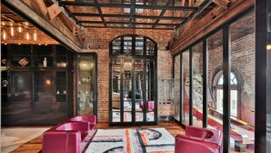 A spacious room with exposed brick walls, large windows, and a modern seating area with pink chairs.