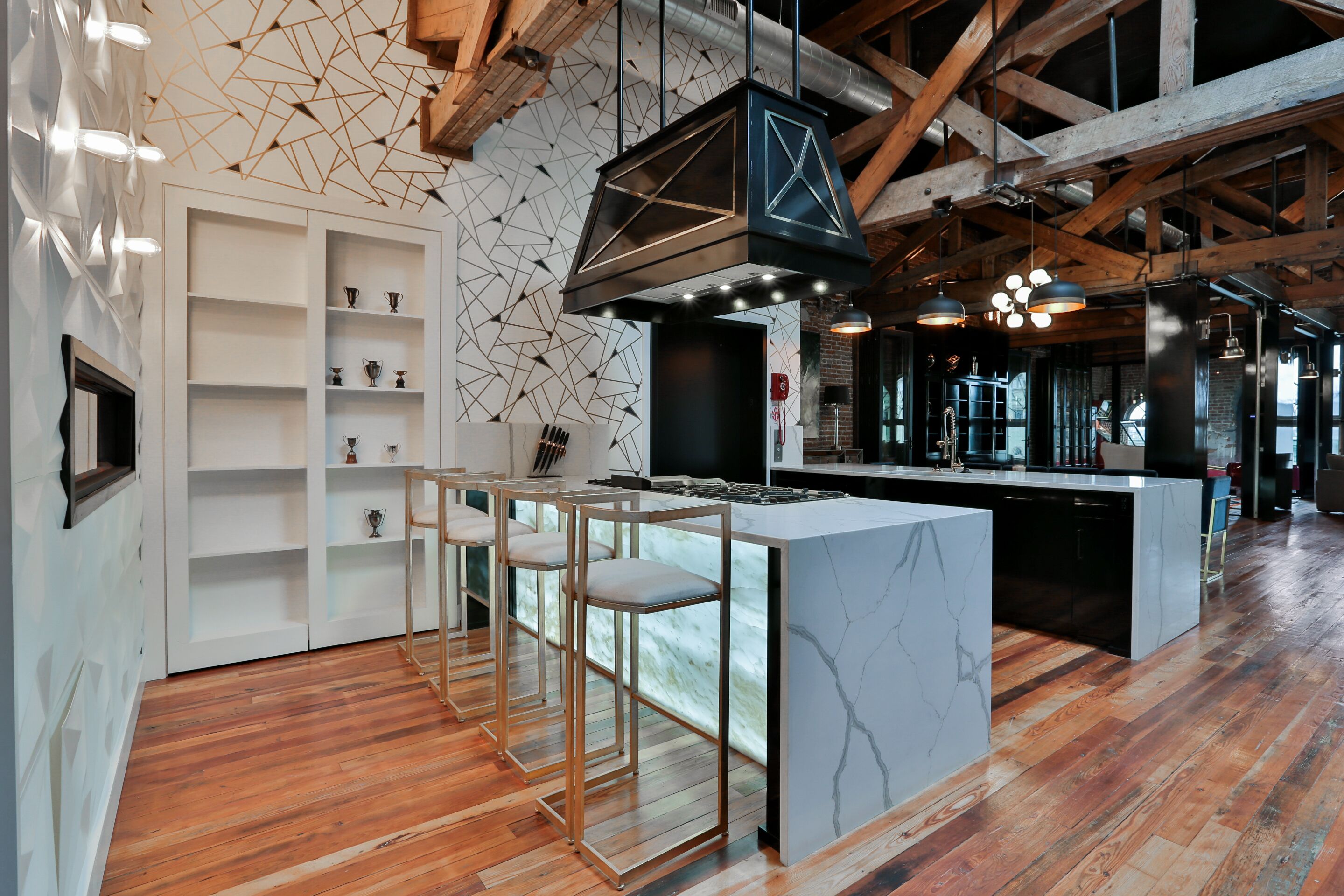 Une cuisine moderne dotée d’un îlot en marbre, de tabourets de bar en bois et d’un motif géométrique sur le mur.