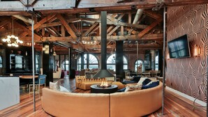 A modern lounge with a curved leather sofa, a central fire feature, exposed wooden beams, and a patterned wall.