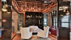 A modern bedroom with a brick wall, a large bed, two white armchairs, and a glass partition.