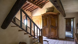 Una habitación con una escalera de madera, un mueble grande de madera y una silla con una mesita.