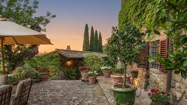 Un patio rústico con suelo de piedra, plantas en macetas y una mesa de madera con sillas.