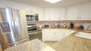 A modern kitchen with white cabinets, stainless steel appliances, granite countertops, and a built-in microwave.