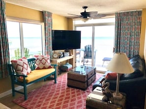 A living room with a sofa, a television, a table, and a view of the ocean.