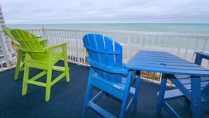 A balcony with two Adirondack chairs, one green and one blue, and a matching table.