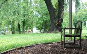 Eine Bank in einem Park mit Bäumen und einem Gewässer im Hintergrund.