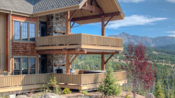 Een houten chalet met twee verdiepingen, een stenen schoorsteen, een balkon en uitzicht op de bergen.