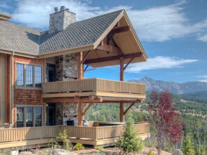 Une cabane en bois à deux étages, dotée d’une cheminée en pierre, d’un balcon et offrant une vue sur la montagne.