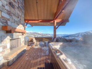 A wooden deck with a stone wall, a hot tub, and a grill.