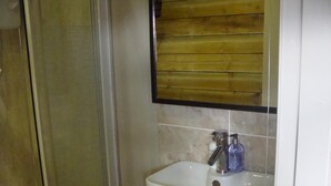Ein Badezimmer mit Duschkabine aus Glas, einem weißen Waschbecken mit Holzablage und einem Spiegel mit Holzrahmen.