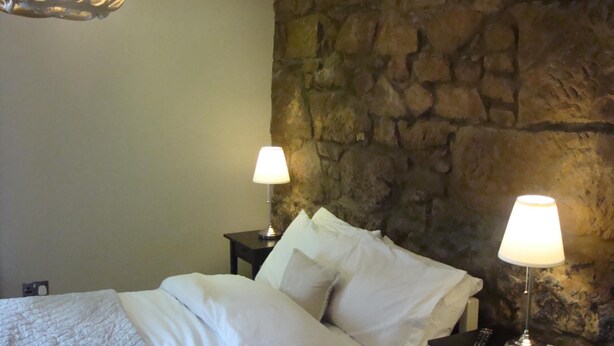 Ein Schlafzimmer mit Steinwand, einem Bett mit weißer Bettwäsche, zwei Nachttischlampen und einer Kandelaberleuchte.