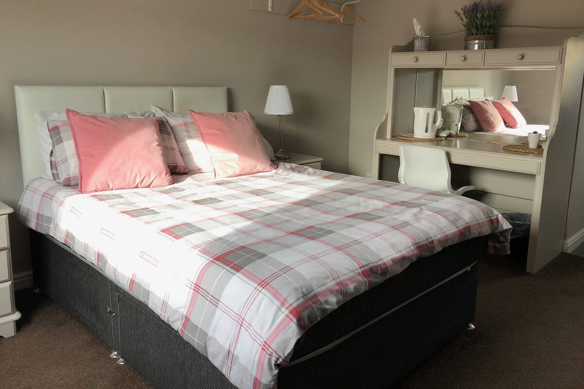 A bedroom with a bed, a desk, a chair, a mirror, and a hanging clothes rack.