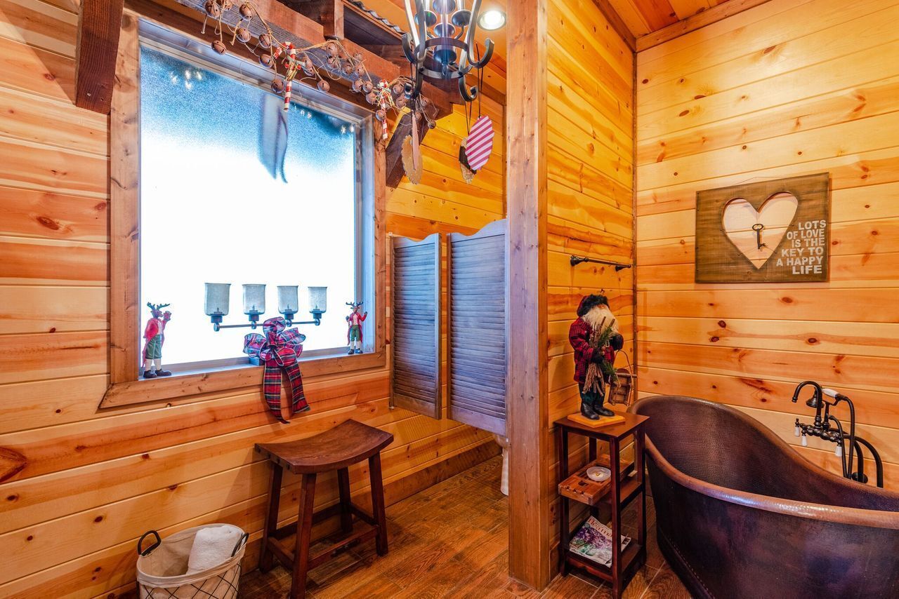 A cozy cabin interior with a wooden interior, a large window with decorations, a bathtub, and a heart-shaped sign on the wall.