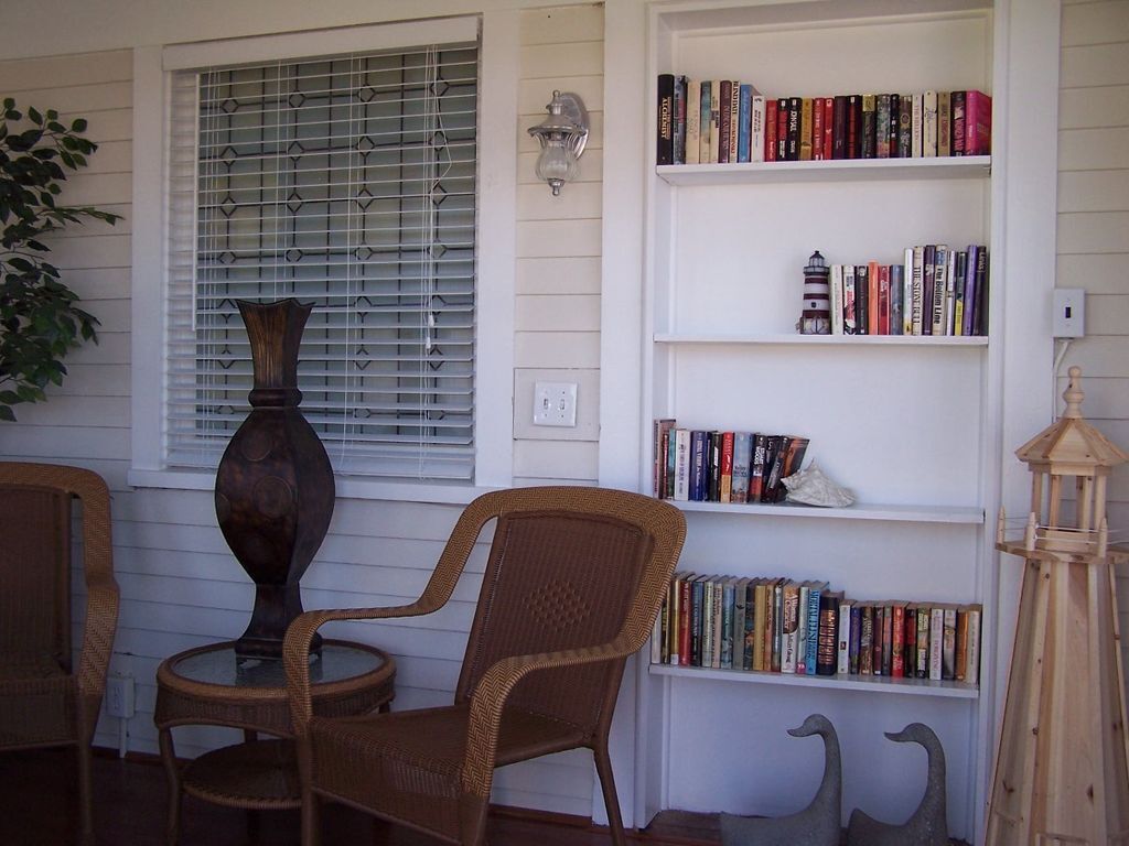 A room with a bookshelf, two wicker chairs, a large vase, and a swan sculpture.