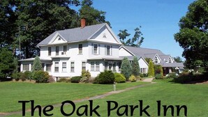 Una casa grande y blanca de dos pisos, con un césped bien cuidado y árboles al fondo, identificada como The Oak Park Inn.